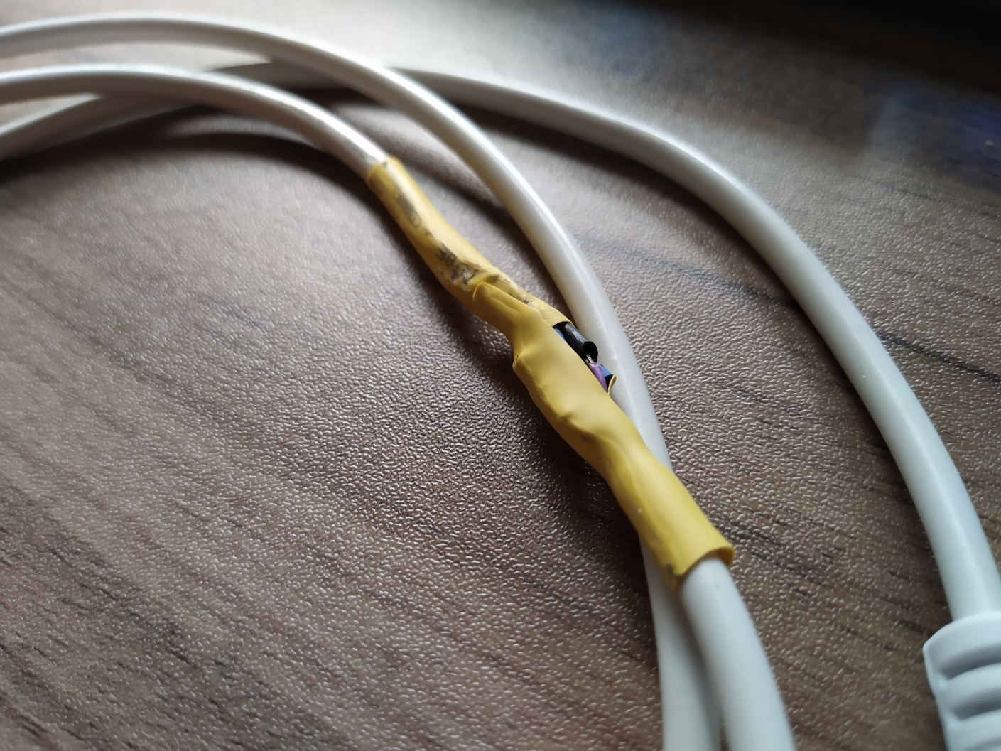 Yellow heatshrink covers a solder joint in a cream serial cable.